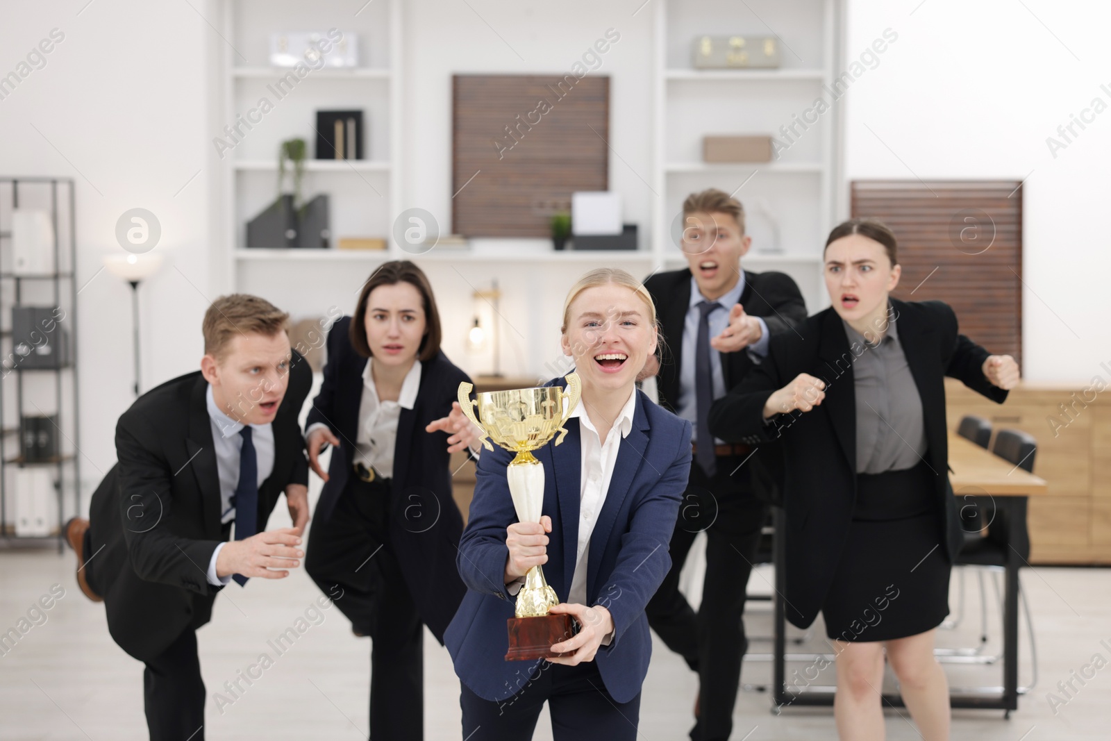 Photo of Competition concept. Happy businesswoman with trophy cup running ahead of her colleagues in office