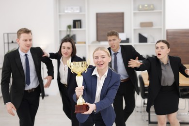 Photo of Competition concept. Happy businesswoman with trophy cup ahead of her colleagues in office