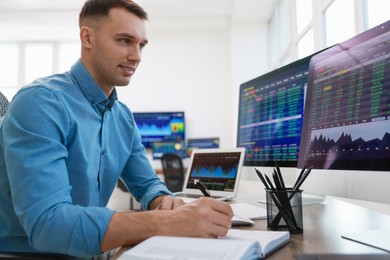 Financial trading specialist writing notes at table in office