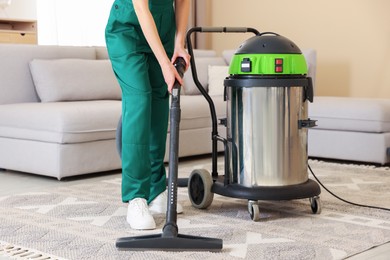 Photo of Professional cleaning service worker vacuuming rug indoors, closeup