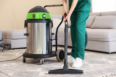 Photo of Professional cleaning service worker vacuuming rug indoors, closeup