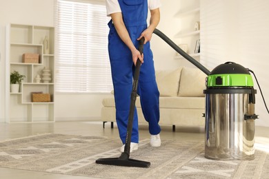 Cleaning service worker vacuuming rug with professional hoover at home, closeup