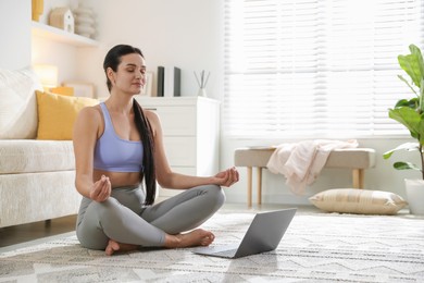 Woman with laptop meditating on floor at home. Space for text