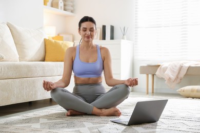 Woman with laptop meditating on floor at home