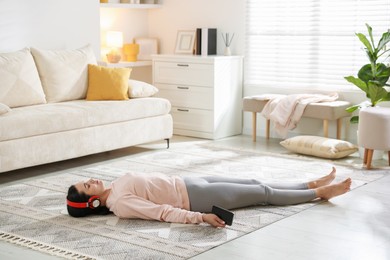 Woman with smartphone meditating on floor at home