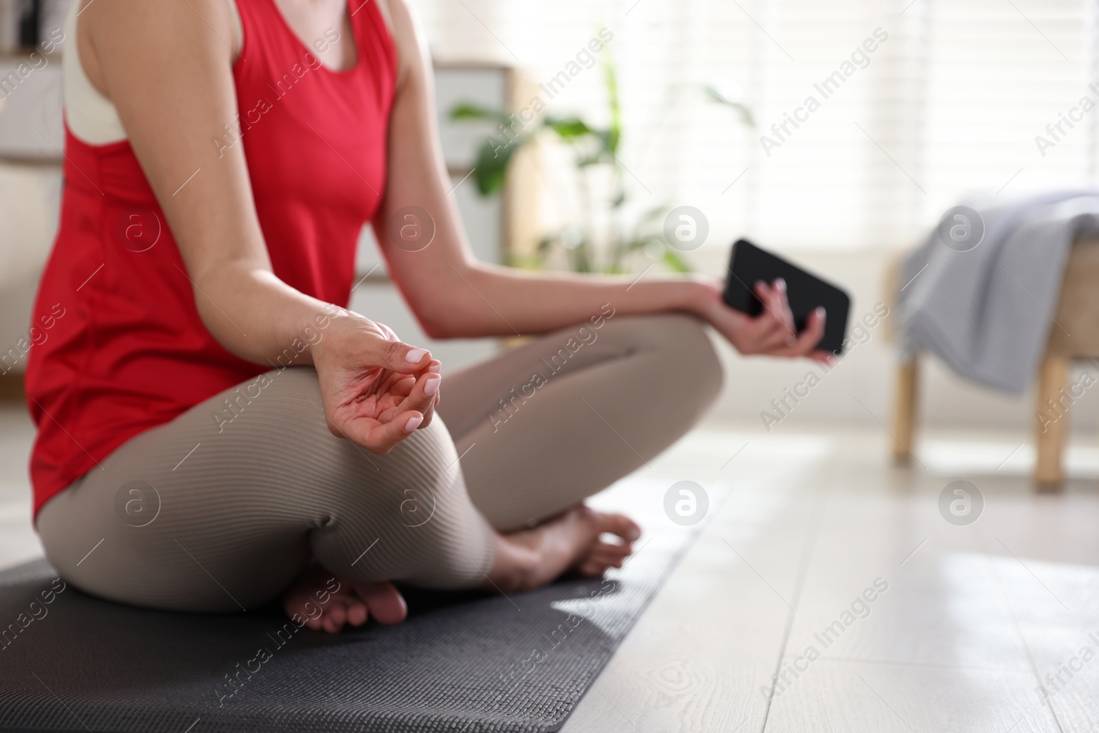 Photo of Woman with smartphone meditating on floor at home, closeup