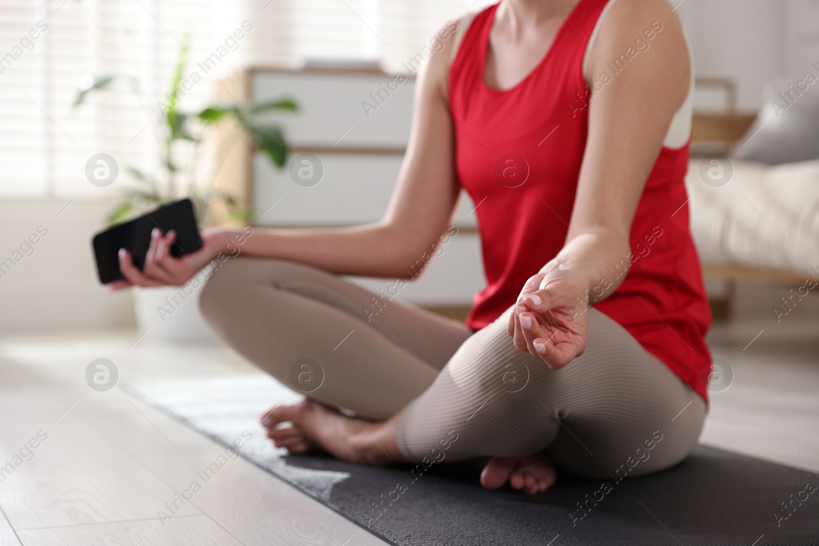 Photo of Woman with smartphone meditating on floor at home, closeup