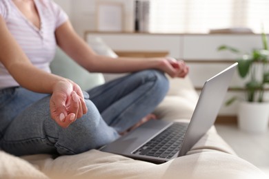 Woman with laptop meditating on sofa at home, closeup