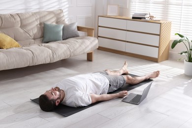 Man meditating near laptop on floor at home