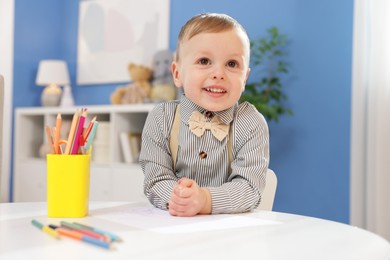 Little boy with colorful pencils at table indoors