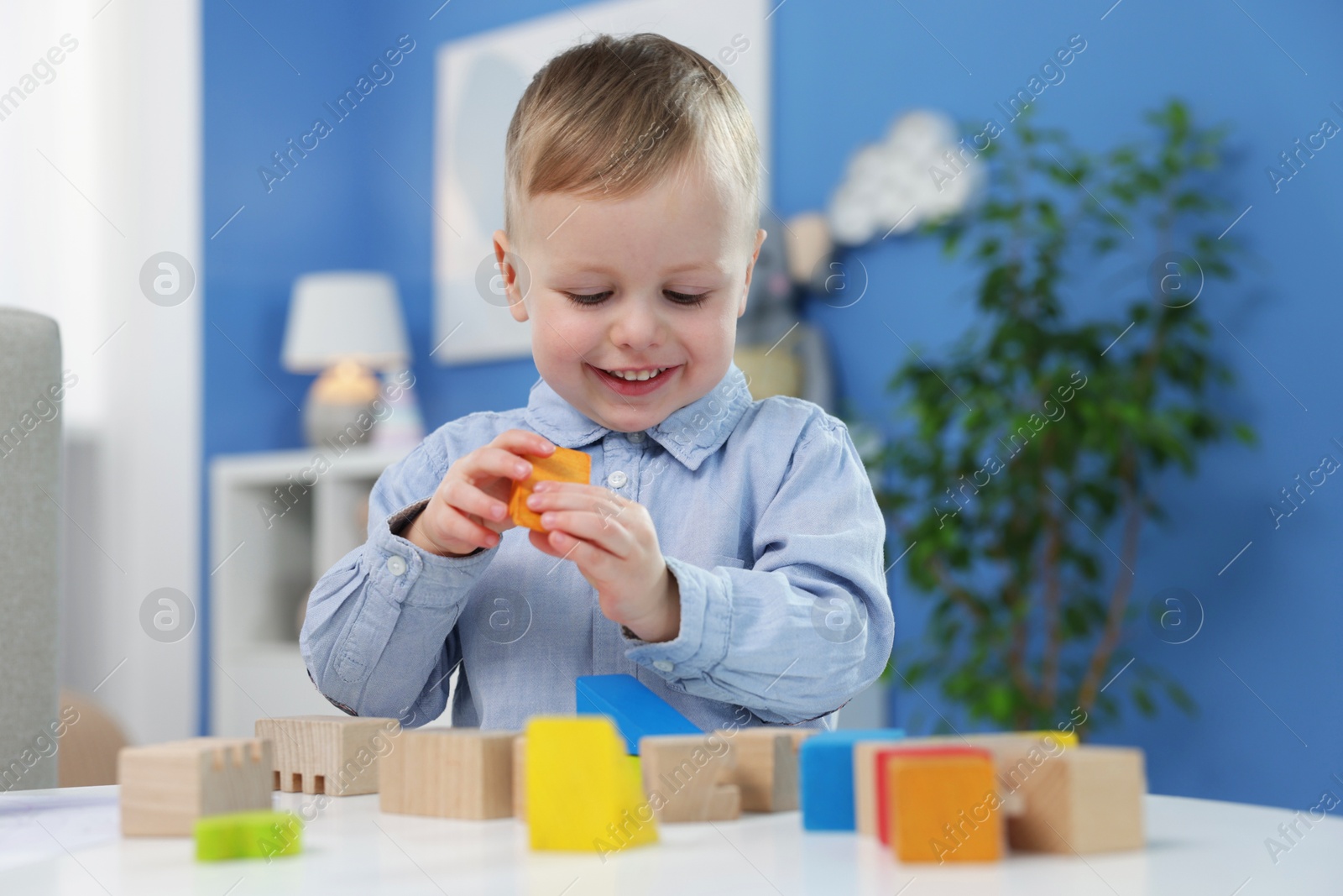 Photo of Little boy playing with wooden blocks at table indoors