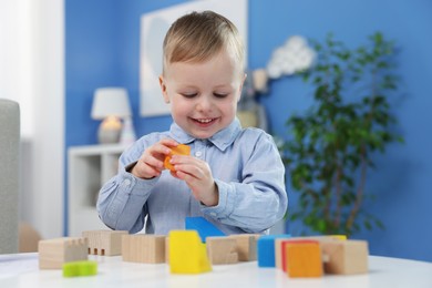 Photo of Little boy playing with wooden blocks at table indoors