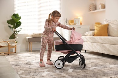 Photo of Cute little girl with doll stroller at home