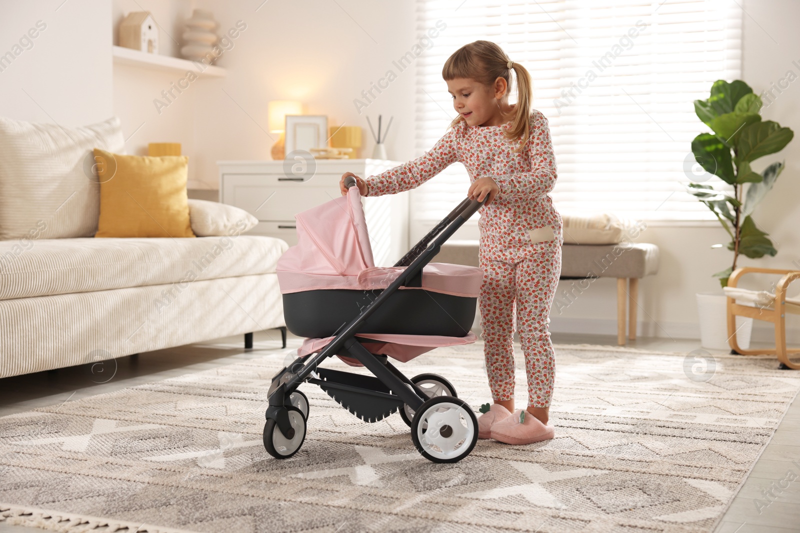 Photo of Cute little girl with doll stroller at home