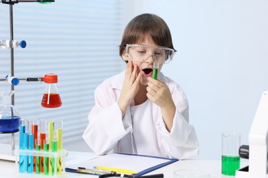 Photo of Little boy doing chemical experiment at desk indoors