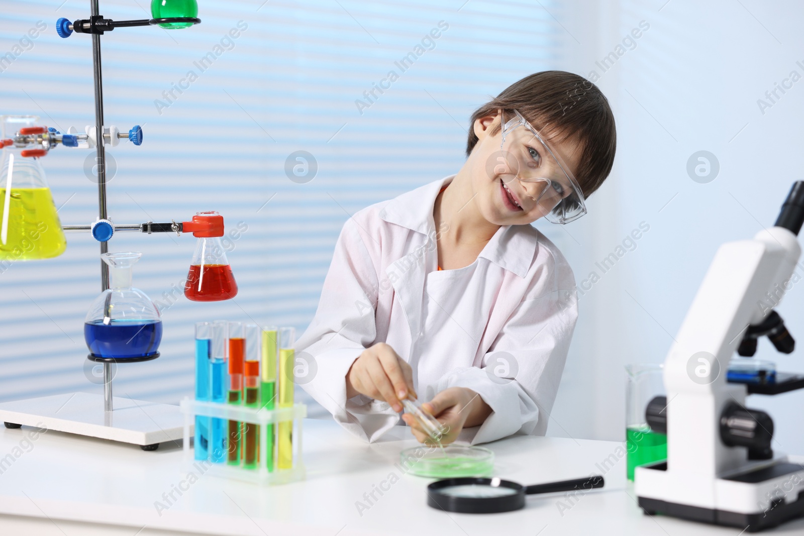 Photo of Little boy doing chemical experiment at desk indoors