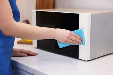 Photo of Woman cleaning microwave oven with rag indoors, closeup