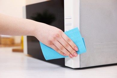 Photo of Woman cleaning microwave oven with rag indoors, closeup