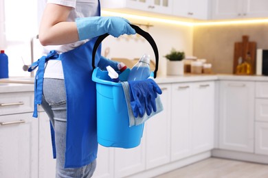 Photo of Woman with bucket with cleaning supplies in kitchen, closeup