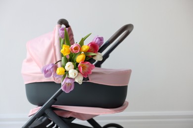 Photo of Stylish doll stroller and tulips near white wall. Kid's toy