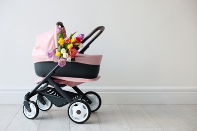 Photo of Stylish doll stroller and tulips near white wall, space for text. Kid's toy