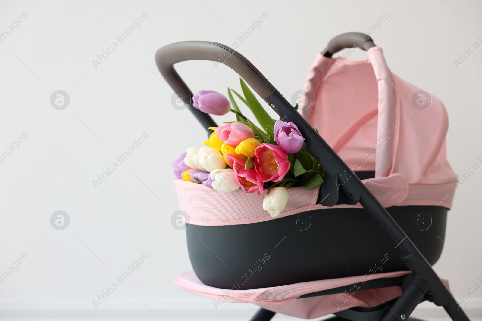 Photo of Stylish doll stroller and tulips near white wall, space for text. Kid's toy