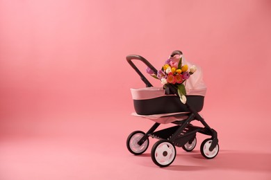 Photo of Stylish doll stroller and tulips on pink background, space for text. Kid's toy