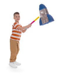 Photo of Happy boy breaking rocket shaped pinata with stick on white background