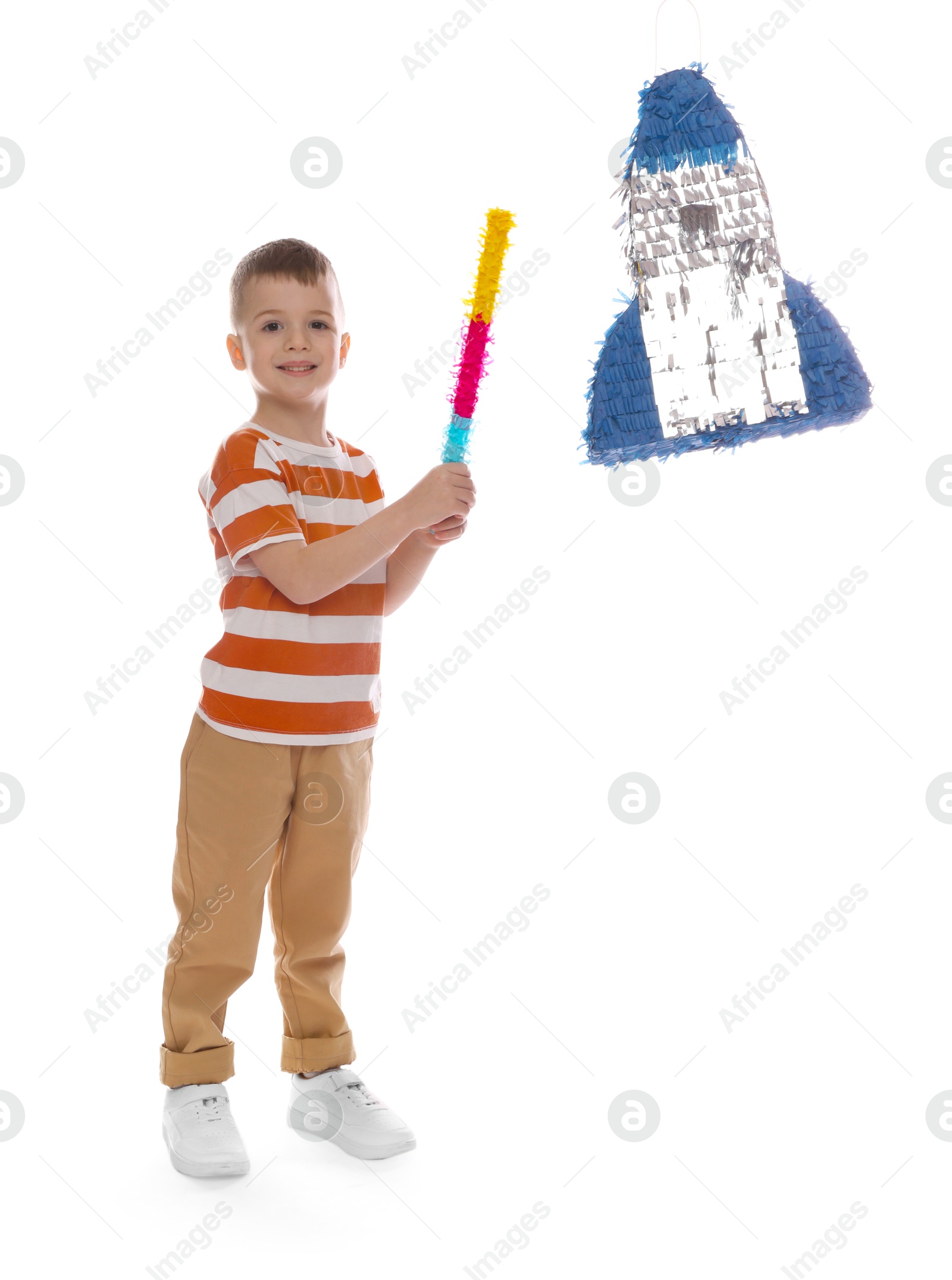 Photo of Happy boy breaking rocket shaped pinata with stick on white background