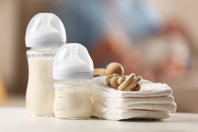 Photo of Mother holding her little baby indoors, focus on feeding bottles with milk, teether and diapers