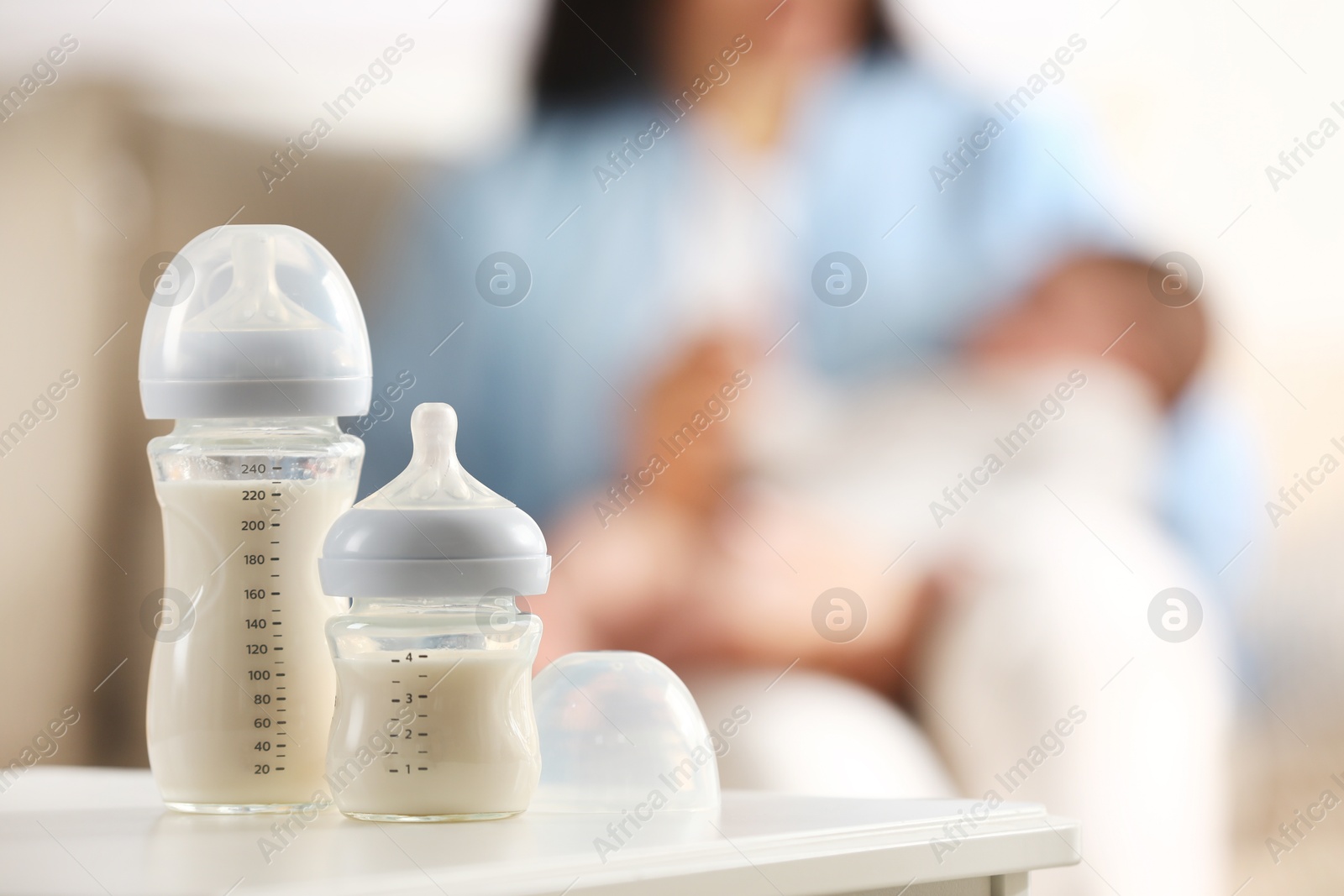 Photo of Mother holding her little baby indoors, focus on feeding bottles with milk