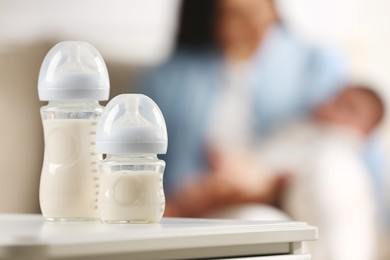 Photo of Mother holding her little baby indoors, focus on feeding bottles with milk