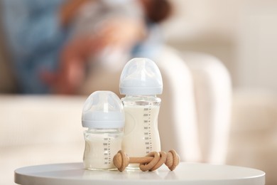 Photo of Mother holding her little baby indoors, focus on feeding bottles with milk and teether