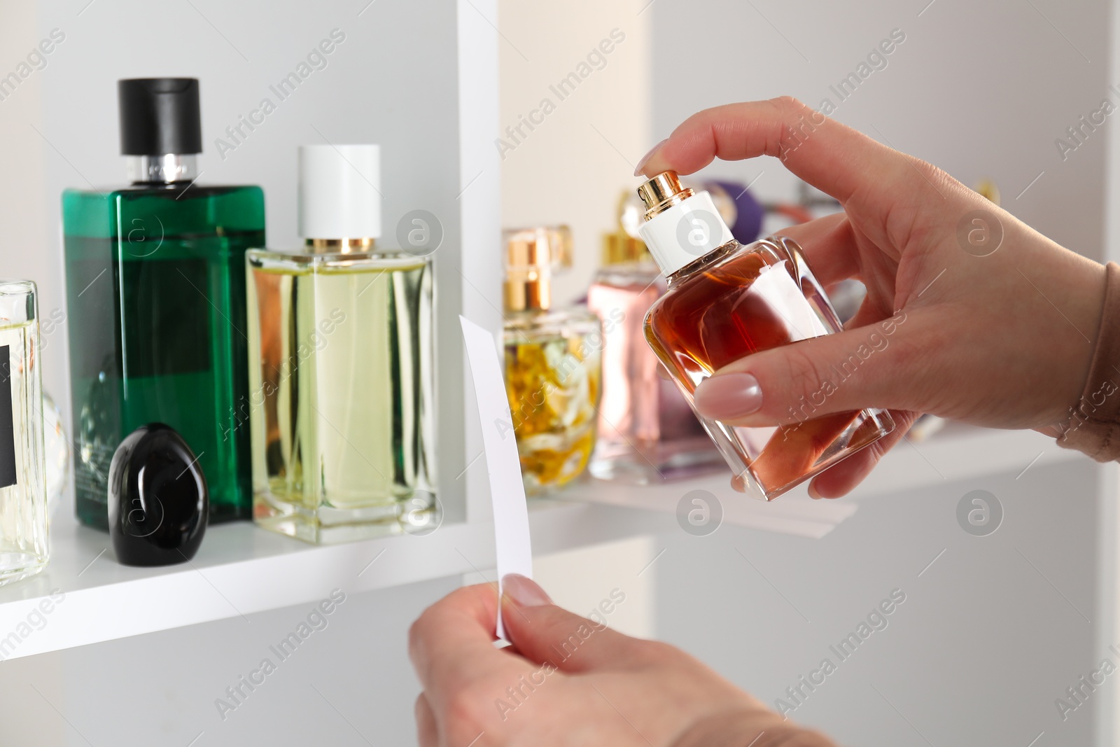 Photo of Woman spraying perfume onto fragrance blotter in store, closeup