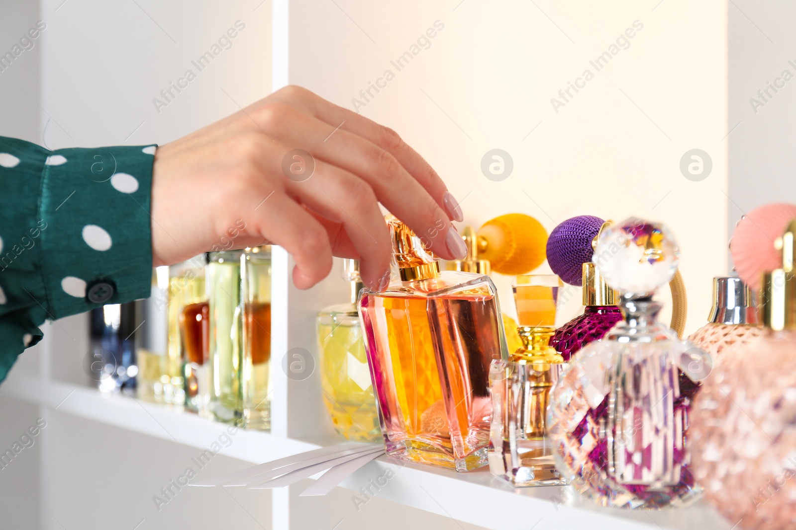 Photo of Woman taking bottle of perfume from shelf in store, closeup