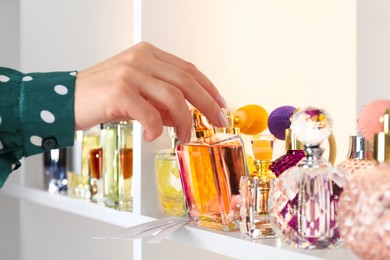 Woman taking bottle of perfume from shelf in store, closeup