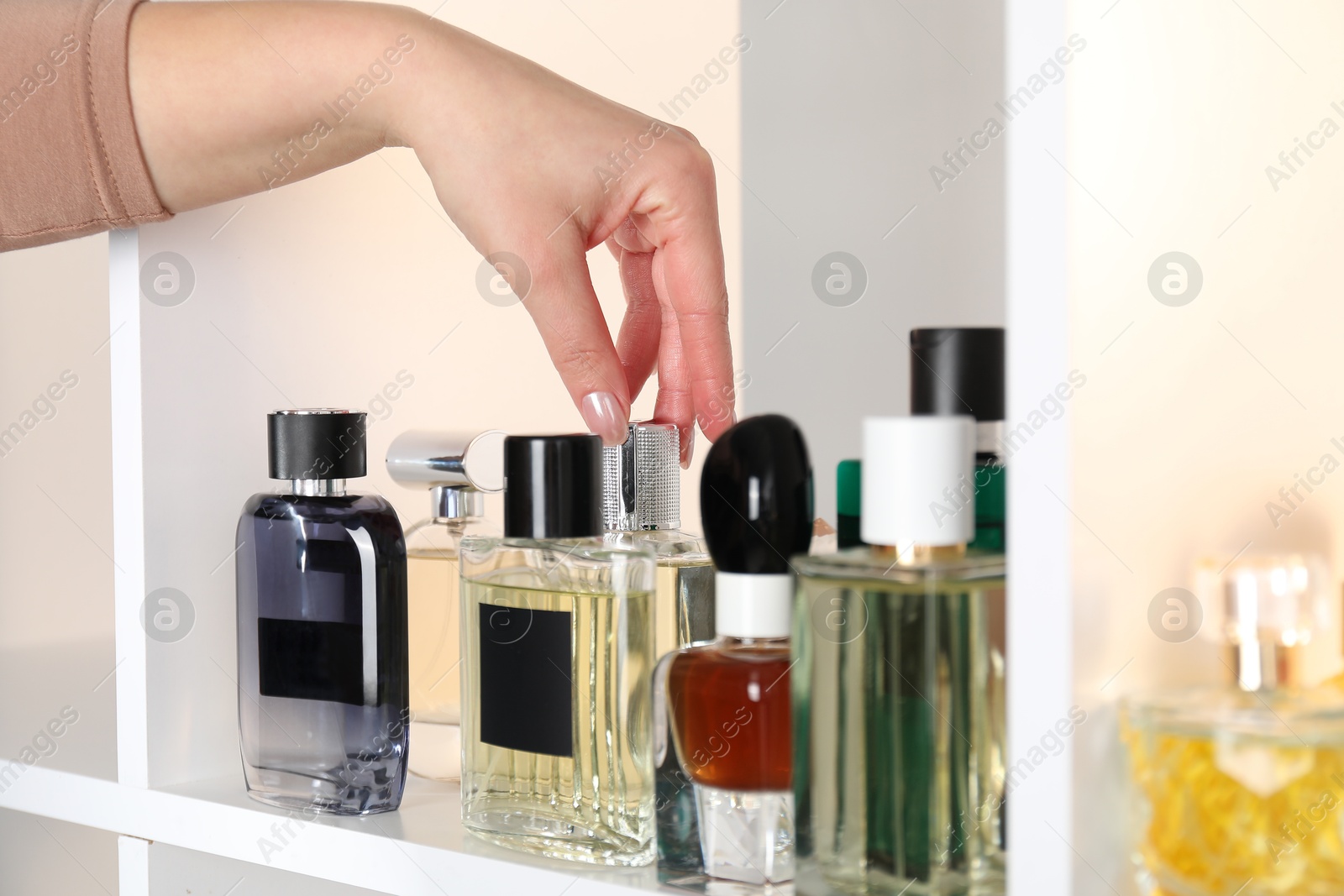 Photo of Woman taking bottle of perfume from shelf in store, closeup