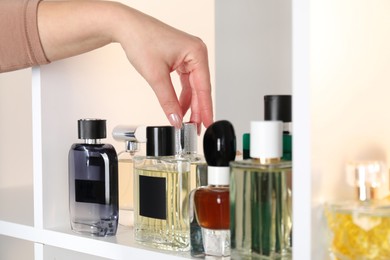 Woman taking bottle of perfume from shelf in store, closeup