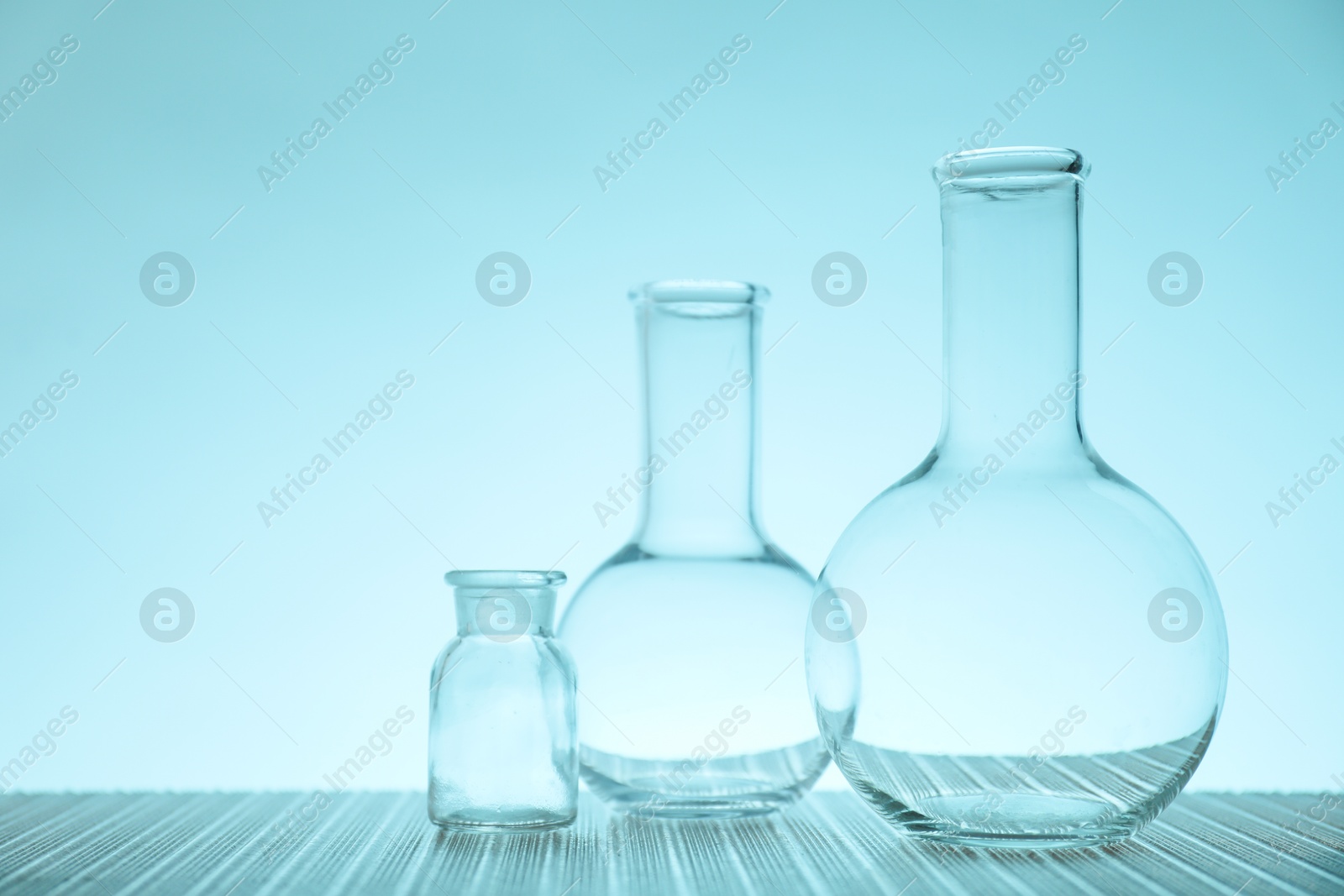 Photo of Empty flasks on table against light blue background, space for text. Laboratory equipment