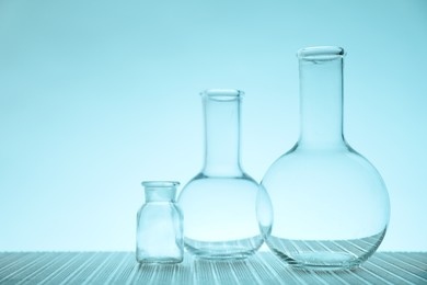 Empty flasks on table against light blue background, space for text. Laboratory equipment