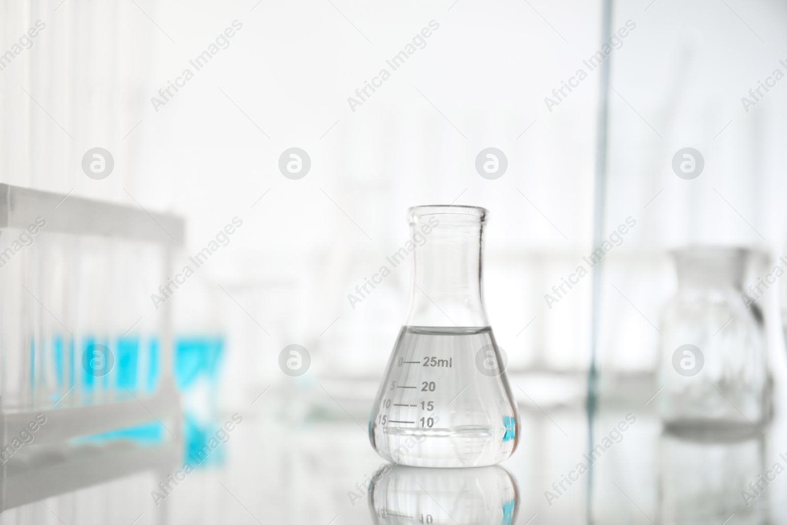 Photo of Flask with liquid on mirror surface against light background. Laboratory glassware