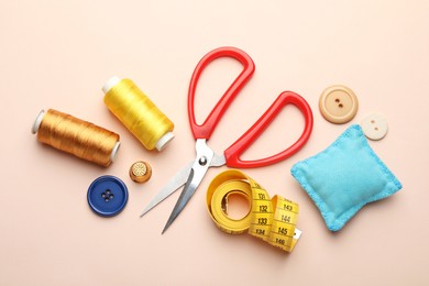 Different sewing supplies on light pink background, flat lay