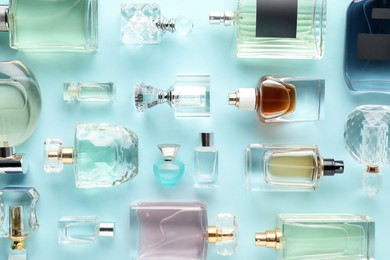 Photo of Bottles of various perfumes on light blue background, flat lay