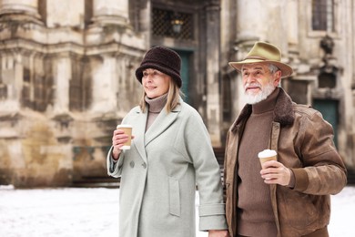 Photo of Happy senior couple with paper cups holding hands on winter day. Space for text