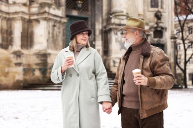 Photo of Lovely senior couple with paper cups holding hands on winter day