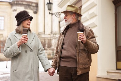 Lovely senior couple with paper cups holding hands on city street