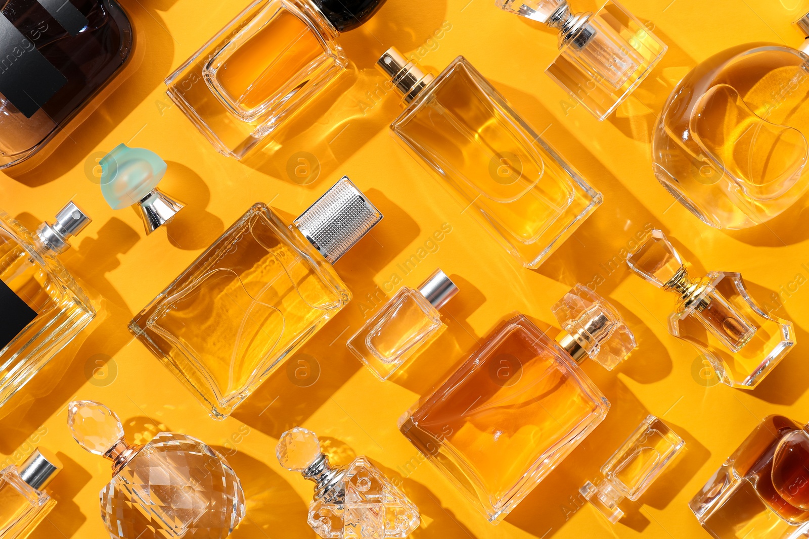 Bottles of various perfumes on yellow background, flat lay Photo of Bottles of various perfumes on yellow background, flat lay