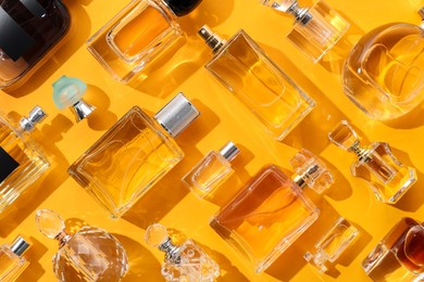 Photo of Bottles of various perfumes on yellow background, flat lay