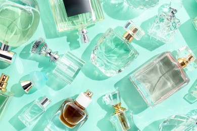 Photo of Bottles of various perfumes on turquoise background, flat lay