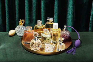 Photo of Different luxury perfumes on green pouf near teal curtains
